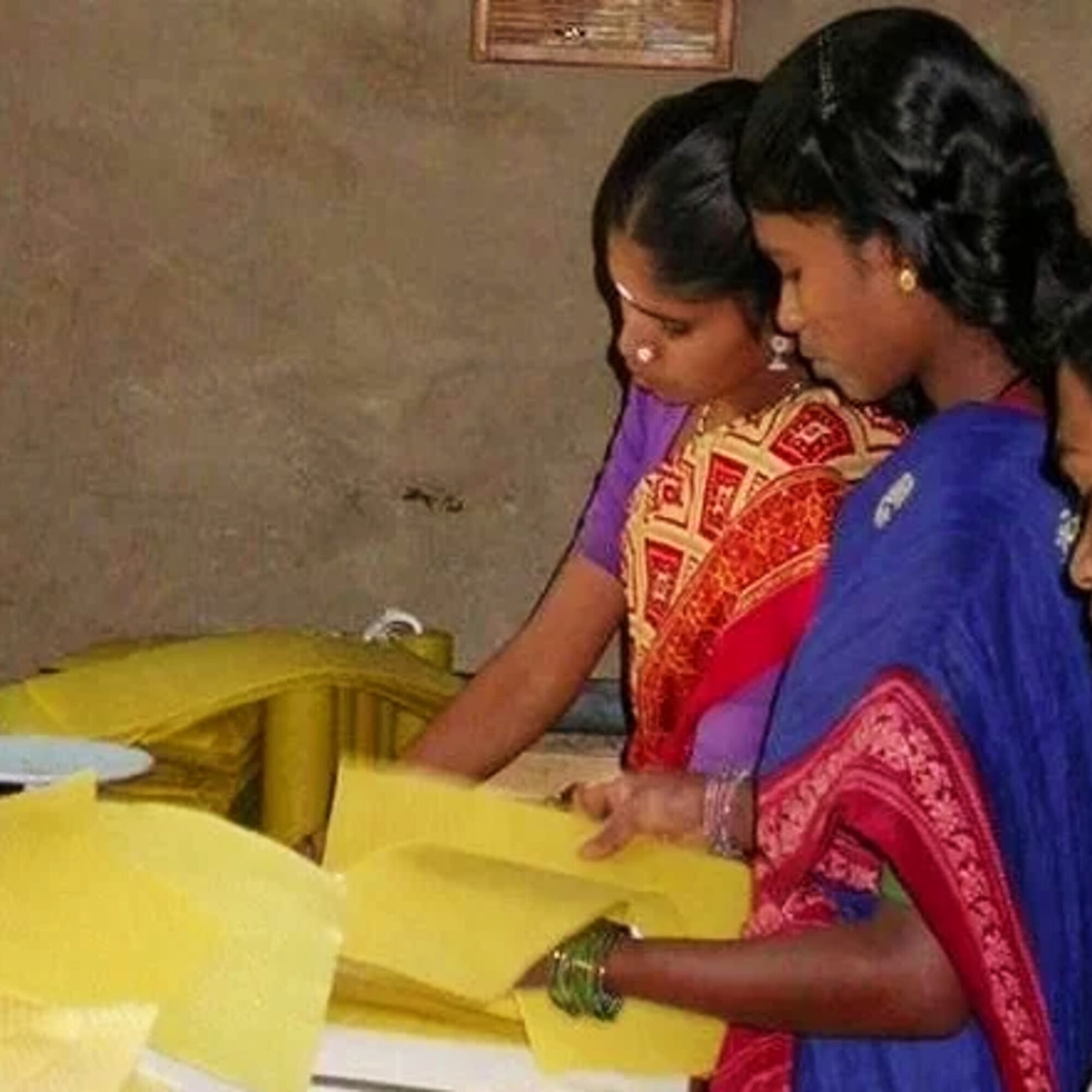 Women handling yellow beeswax sheets at a work table in the Nilgiris