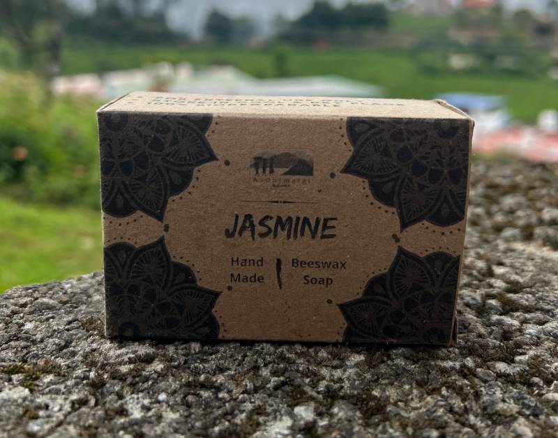 Aadhimalai handmade beeswax soap, Jasmine, 100 g in a printed kraft carton on a stone wall in the Nilgiris — producer's own photograph
