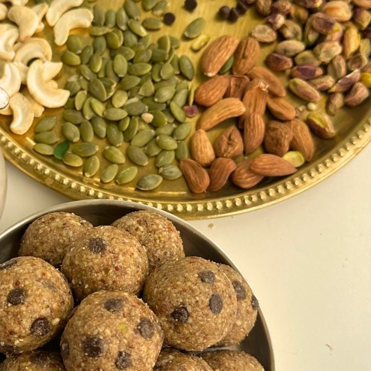 Choco chip laddoos in a steel bowl beside a brass plate of cashews, pumpkin seeds, almonds and pistachios
