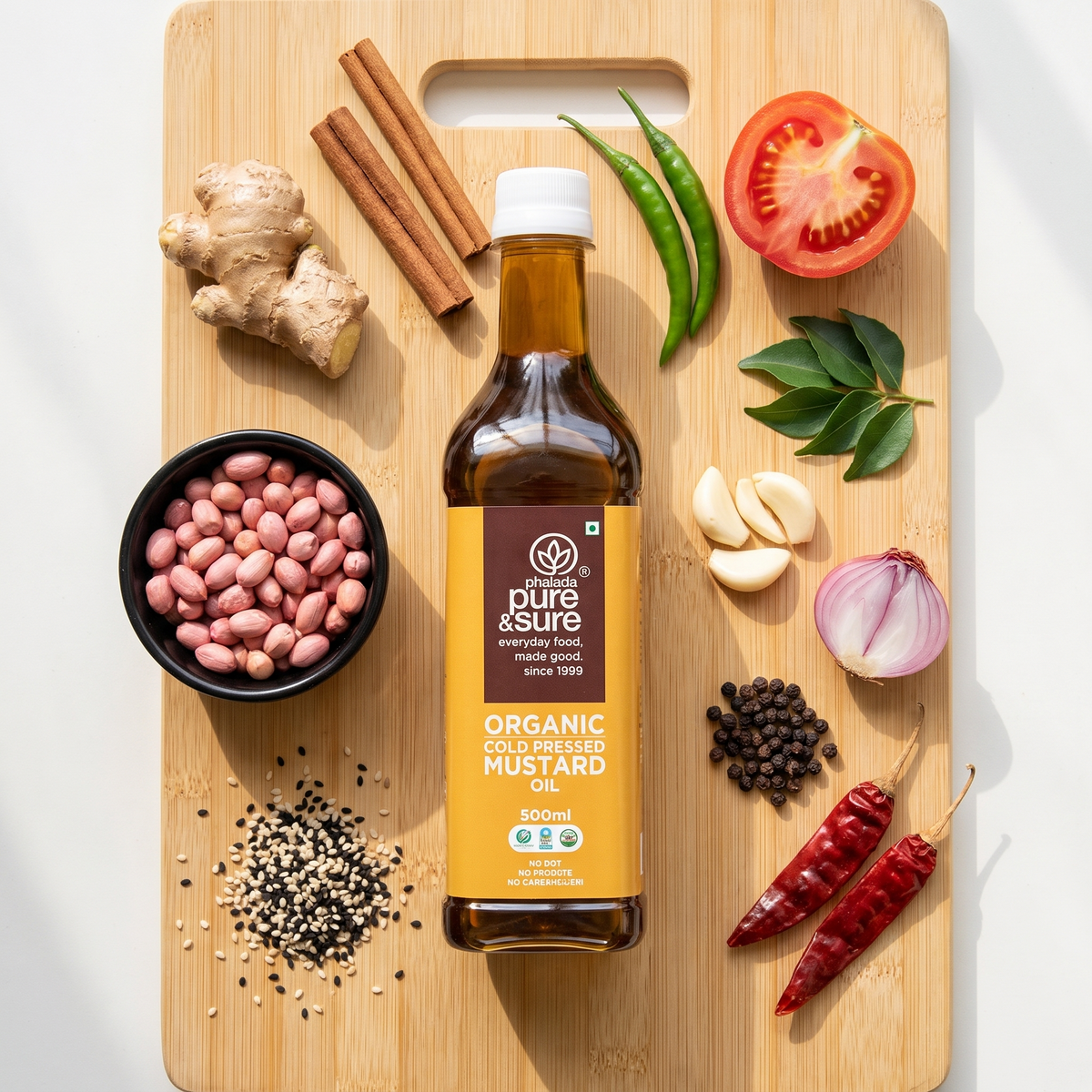 Cold-pressed mustard oil bottle on a bamboo board with groundnuts, ginger, cinnamon, chillies, garlic, shallot, peppercorns and sesame seeds
