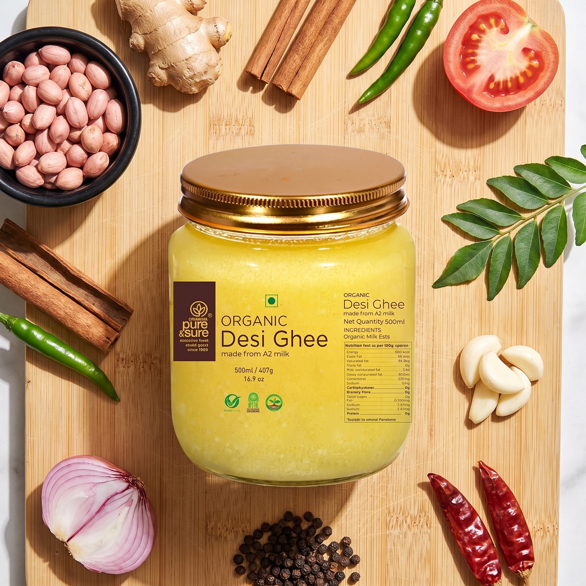Organic A2 desi ghee jar on a bamboo board with groundnuts, ginger, cinnamon, chillies, garlic, shallot and peppercorns