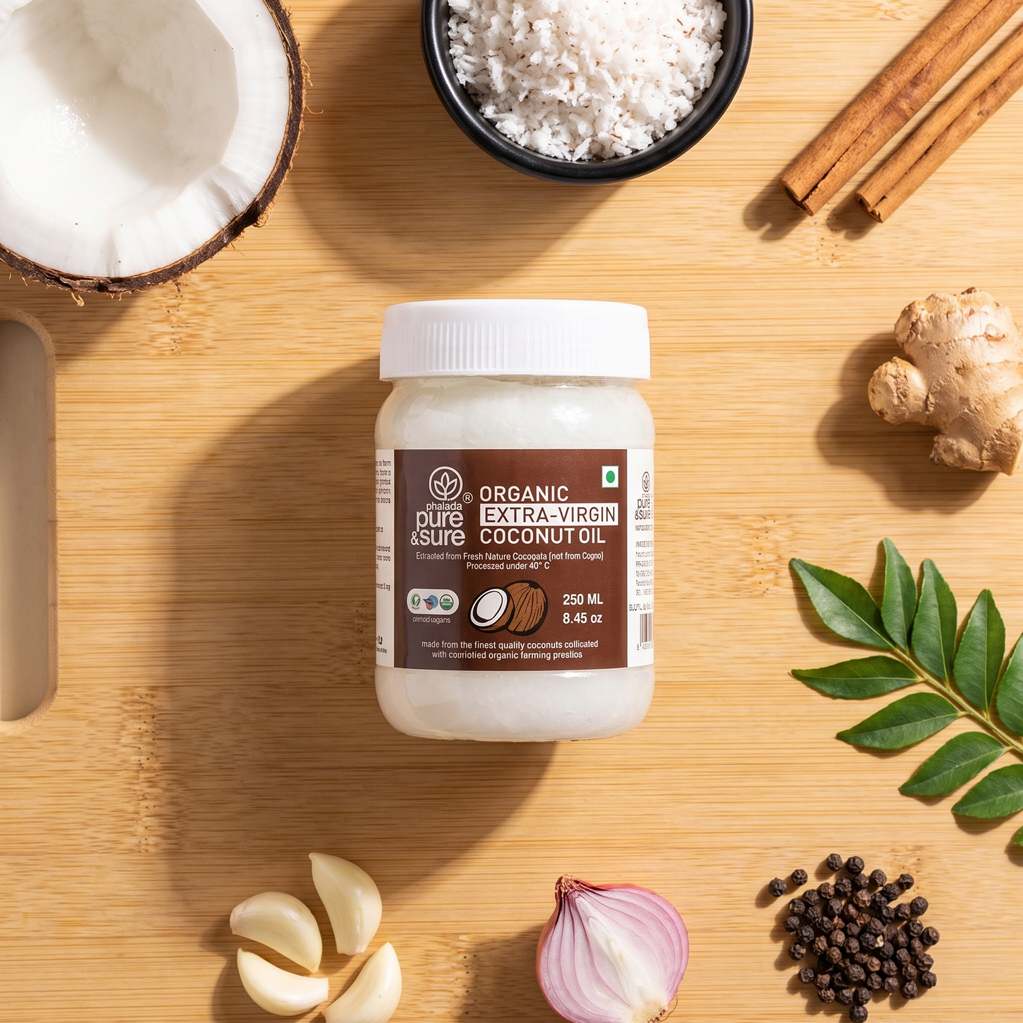Extra virgin coconut oil jar on a bamboo board with fresh coconut, grated coconut, cinnamon, ginger, curry leaves and peppercorns