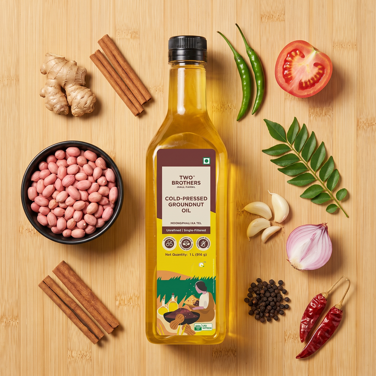 Cold-pressed groundnut oil bottle on a bamboo board with groundnuts, ginger, cinnamon, chillies, garlic, shallot and peppercorns