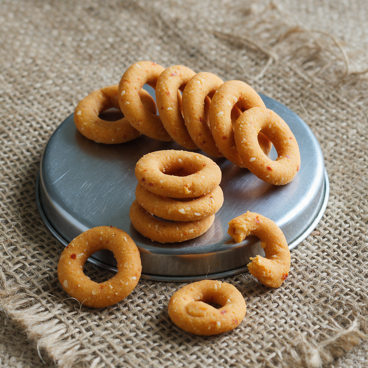 Kodbale rings on a jute placemat, six stood on edge in a row so the holes line up, three stacked flat on a scratched steel dabba lid