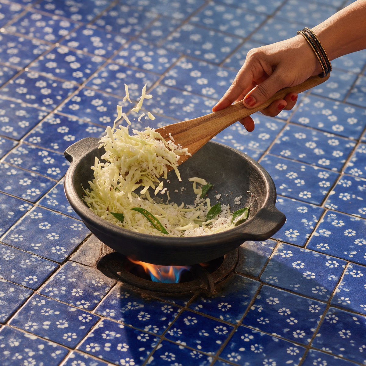 Cabbage and grated coconut tossed with a wooden spatula in a cheena chatti over a gas flame