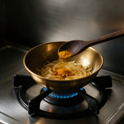 Half a teaspoon of turmeric powder going onto onions in a brass kadhai on a gas burner