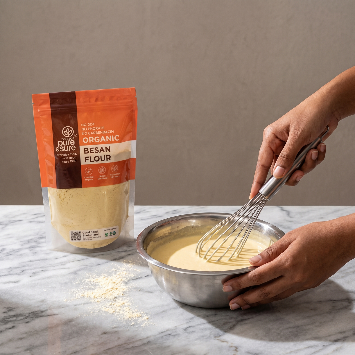 Whisking a smooth besan batter in a steel bowl, with the pack standing on the counter behind
