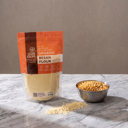 The besan pack standing on a marble counter beside a steel bowl of chana dal, with a scatter of gram flour