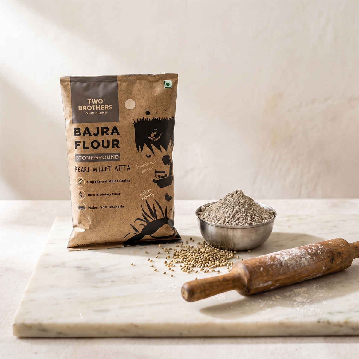 Bajra atta pack on a marble slab with a steel bowl of bajra flour and a rolling pin