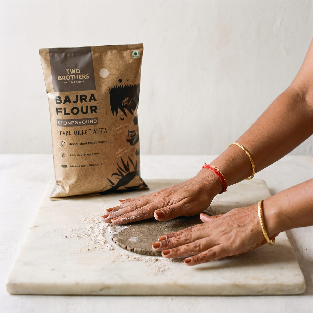 Hands patting out a bajra bhakri on a floured marble slab beside the pack
