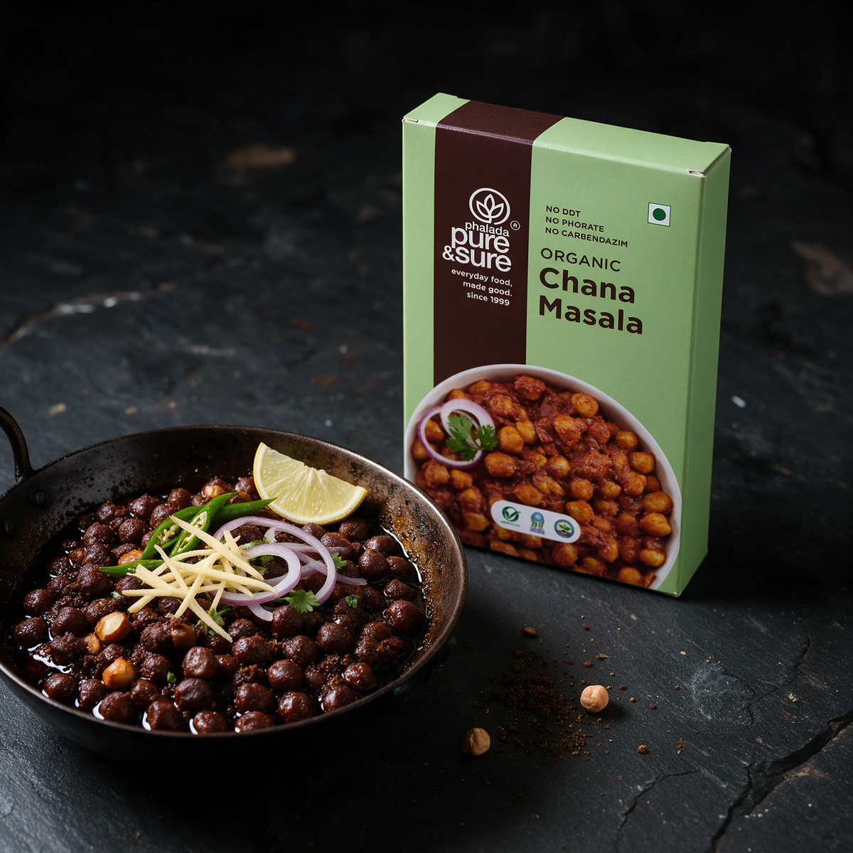 The Pure & Sure chana masala carton beside a karahi of dark pindi chole with ginger juliennes, green chilli, onion and lemon