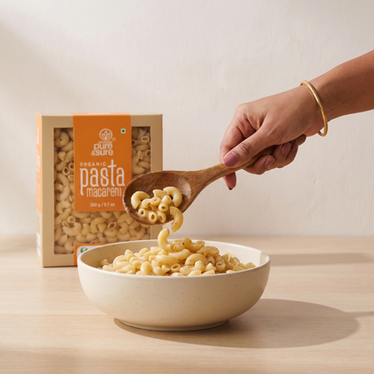 Cooked macaroni being served into a bowl with a wooden spoon, the pack standing on the counter behind