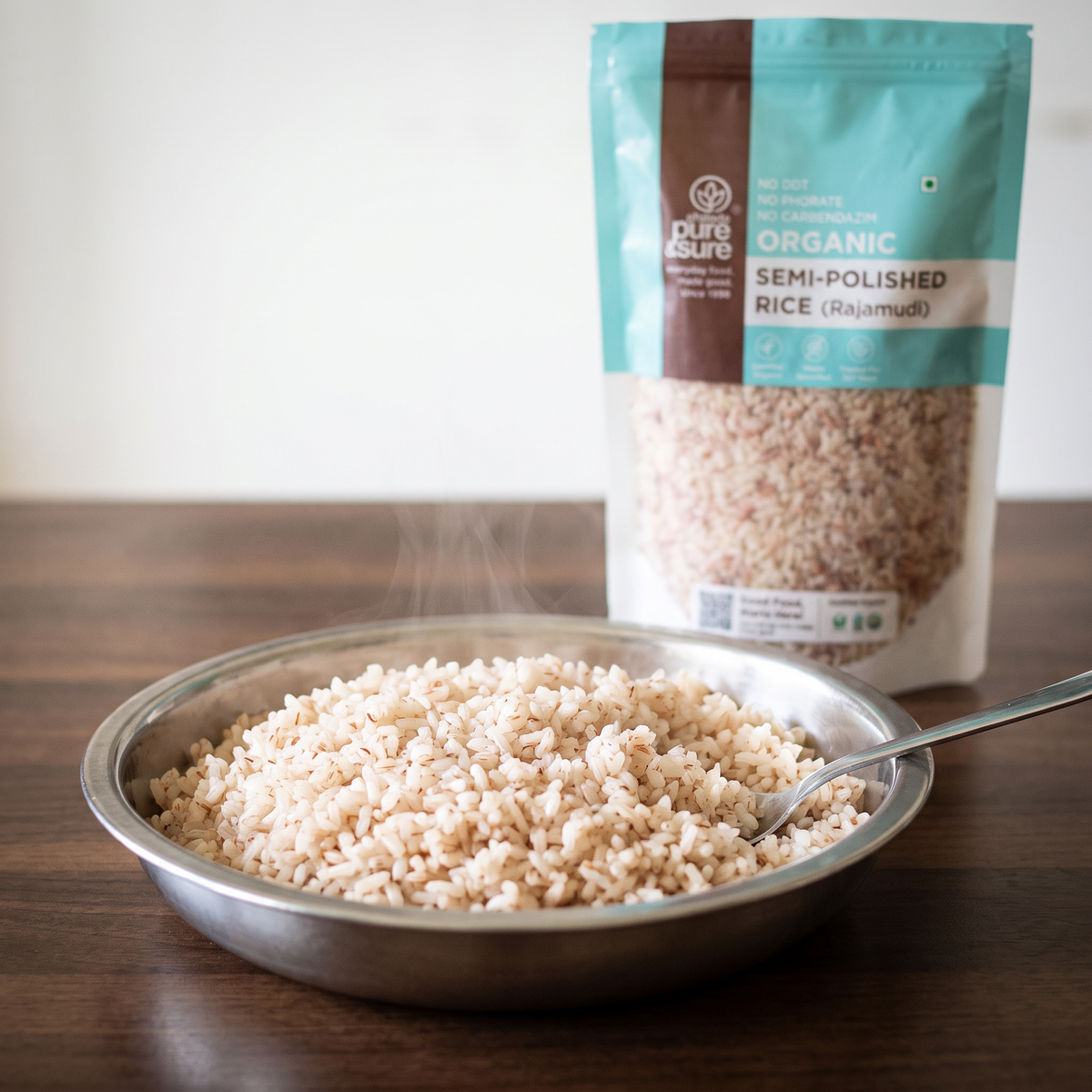 Freshly cooked semi-polished Rajmudi rice steaming in a steel bowl with the pack behind