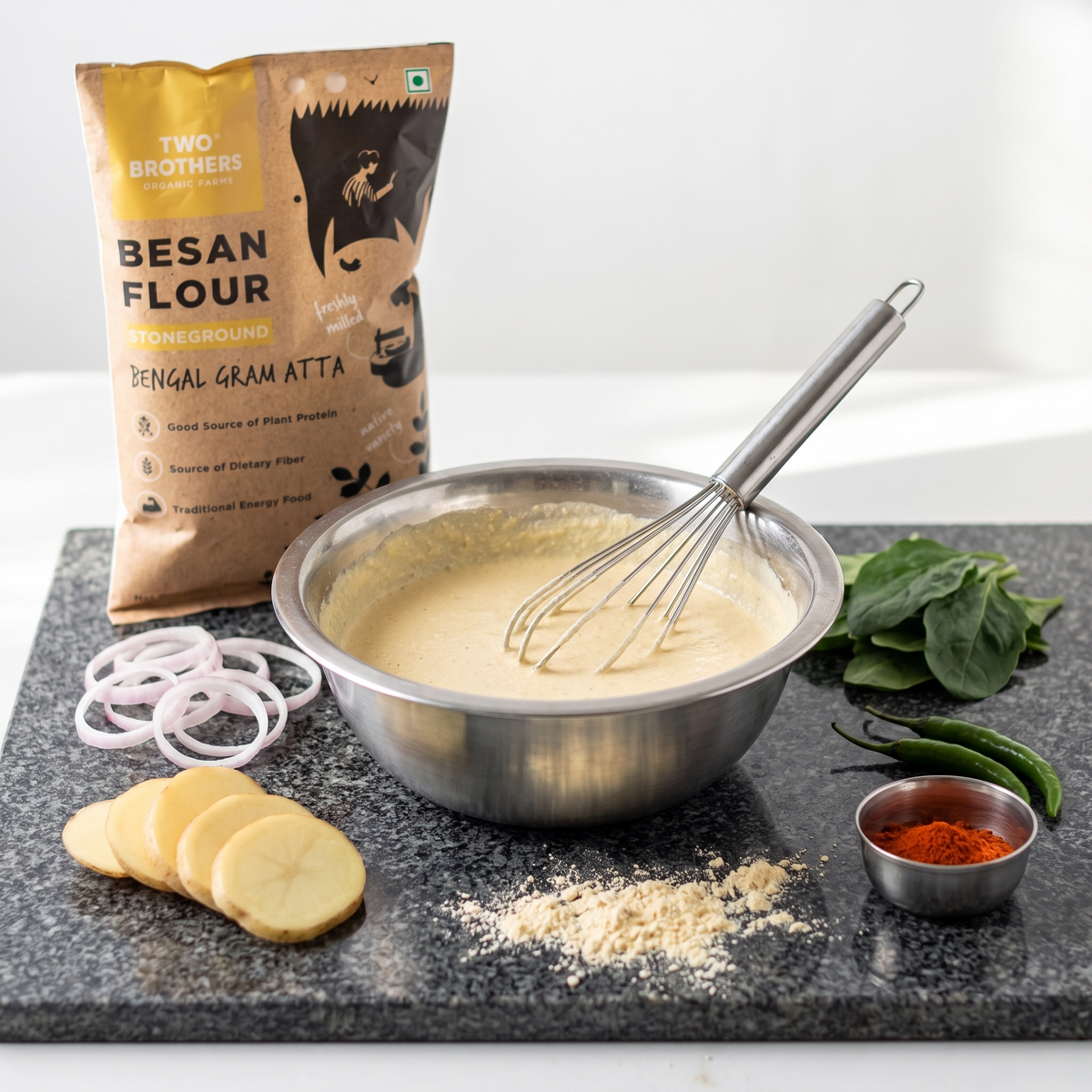 Besan batter whisked in a steel bowl with onion, potato, spinach and chilli ready for pakoras, the pack behind