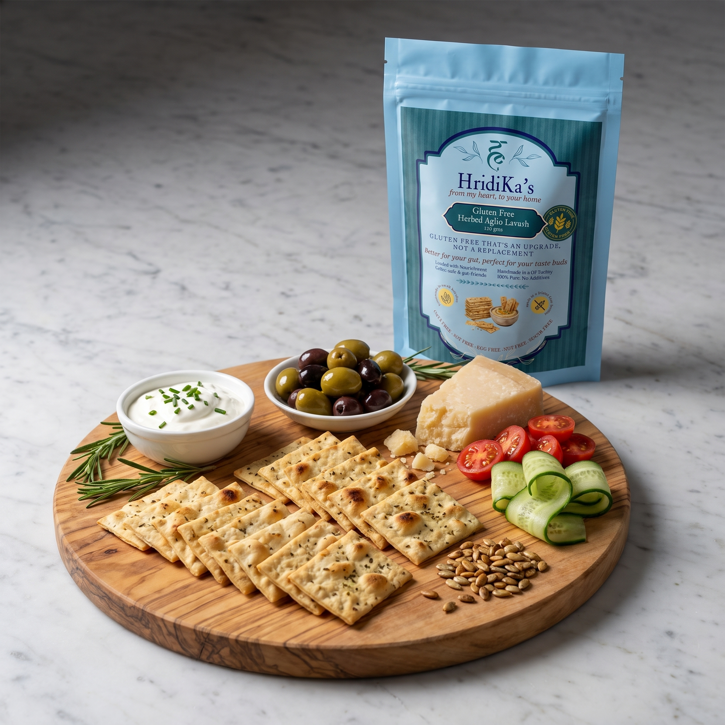 A grazing platter of HridiKa's gluten free herbed aglio lavash crackers with olives, aged cheese, tomatoes, cucumber and chive sour cream, the pack standing behind