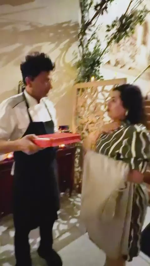 Video of a person in an apron holding out an open red gift box to a guest at an evening event