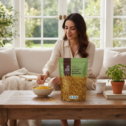 purepicked Aloo Bhujia snack in a green pouch on a wooden table with a woman snacking in a bright living room