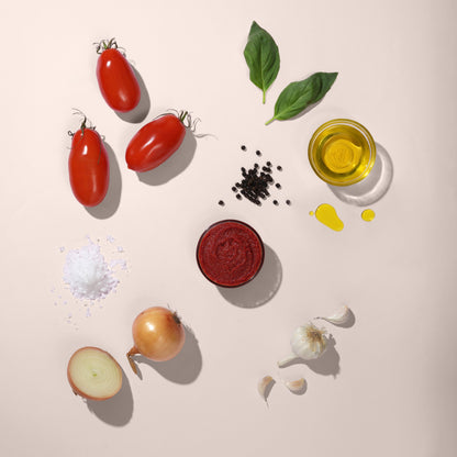purepicked Classic Marinara sauce in a jar surrounded by fresh San Marzano tomatoes, garlic, basil, and olive oil.