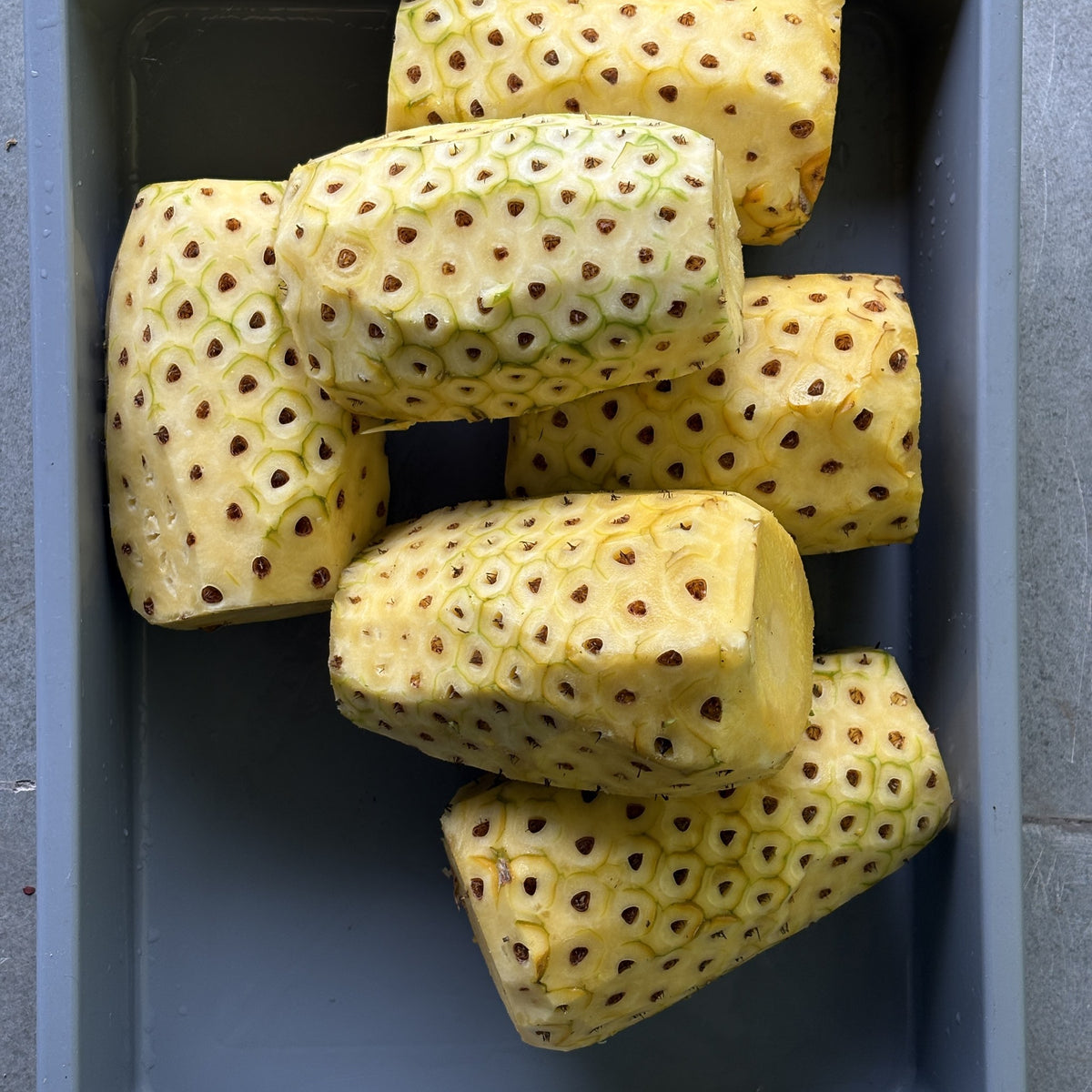 Whole pineapples, peeled by hand, in a tray at Smunchie before slicing