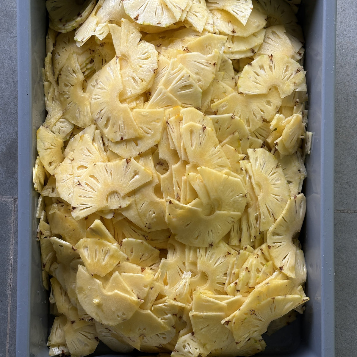 Fresh pineapple sliced thin in a tray at Smunchie, before drying